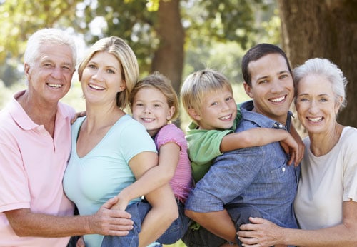 A family of six smiling and standing close together in a beautiful park, enjoying a day outdoors.